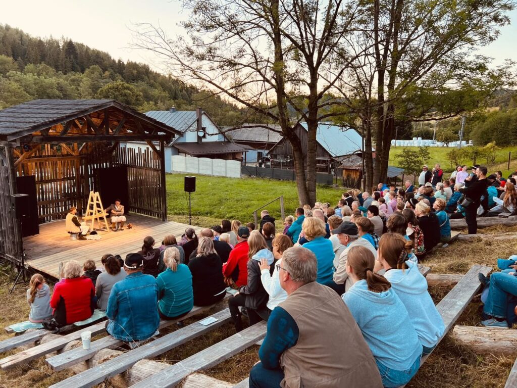 Professional actors on the wooden open-air stage at Zogrod, audience seated on the hillside